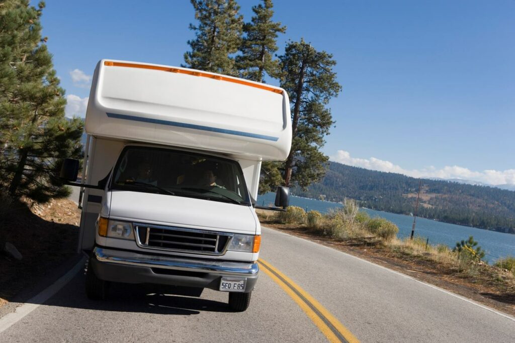 An RV driving along a mountain road beside a lake.