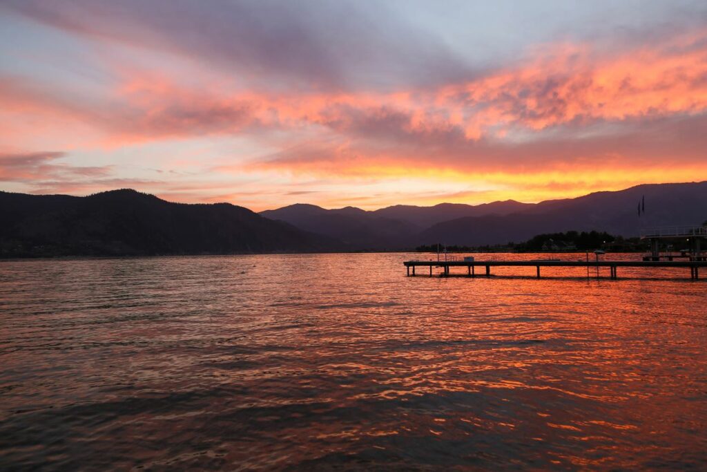 A sunset waterfront view of a dock on Lake Chelan, with a silhouette of mountains.