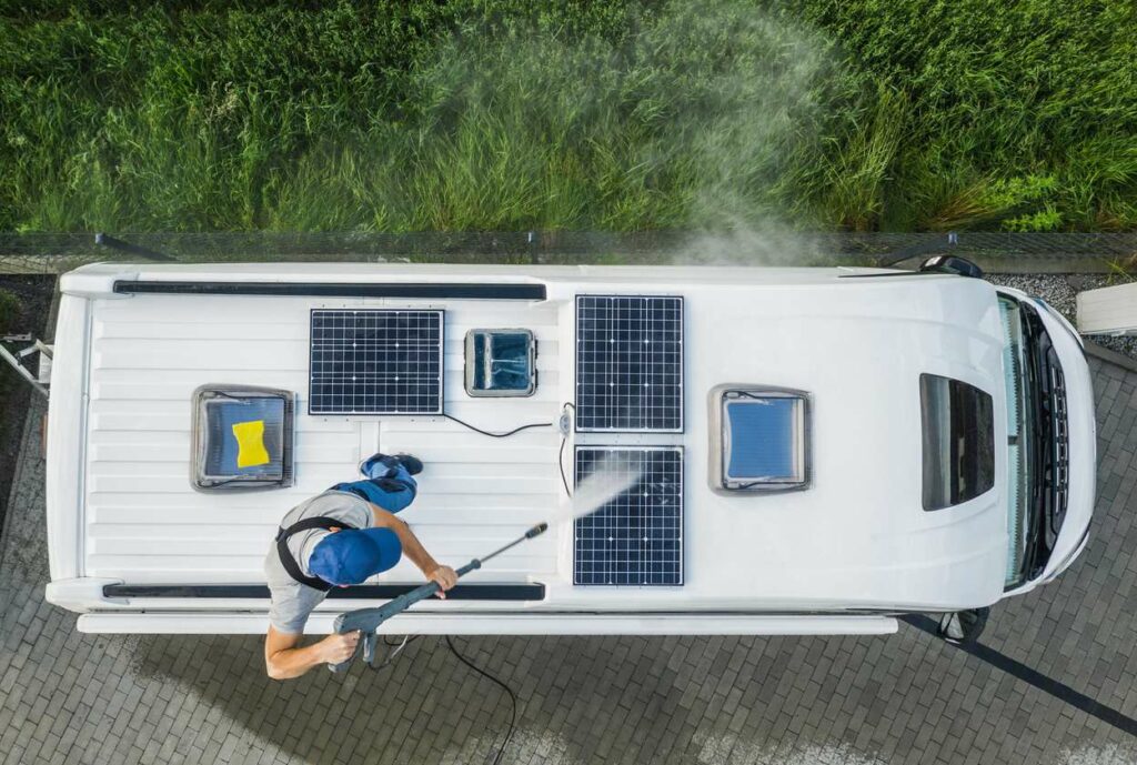 A bird’s-eye view of a man pressure washing the roof of an RV camper parked on a driveway.