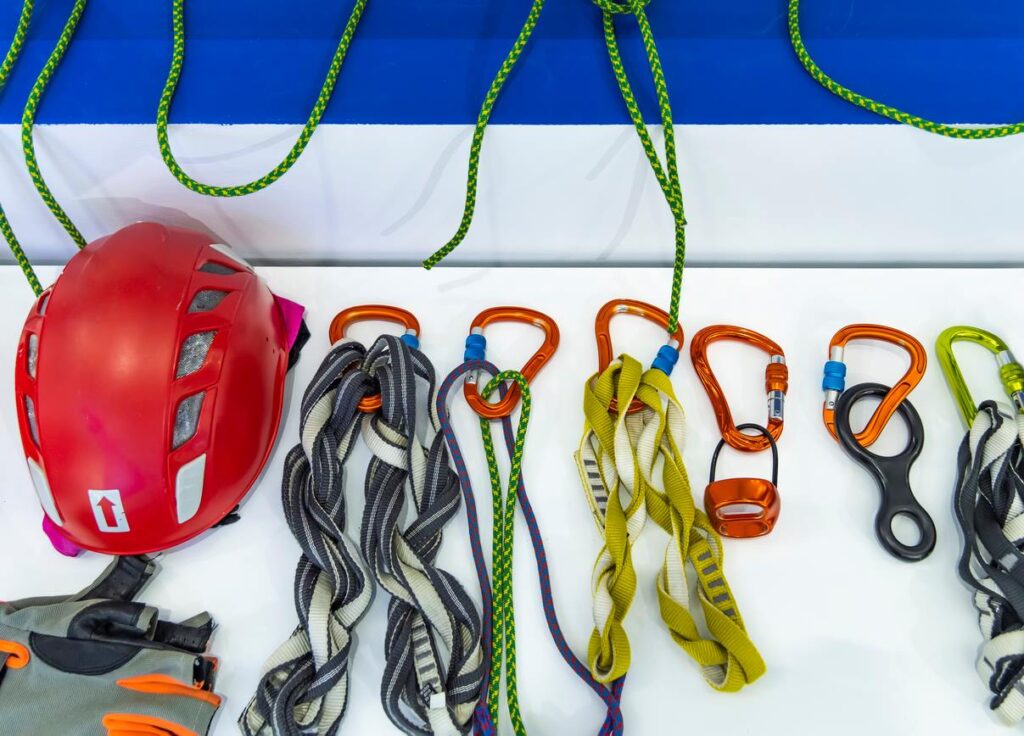 Outdoor recreational gear including a helmet, life jacket, carabiners, and ropes hanging on a wall.