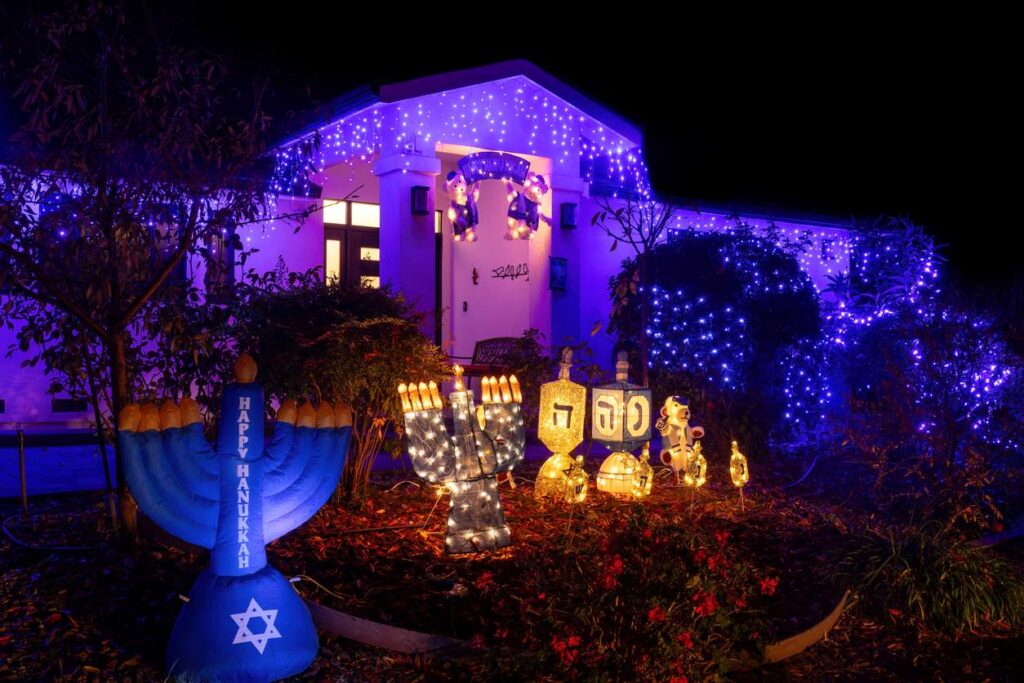 A house decorated with lights, decorative dreidels, and an inflatable menorah to celebrate Hanukkah. 