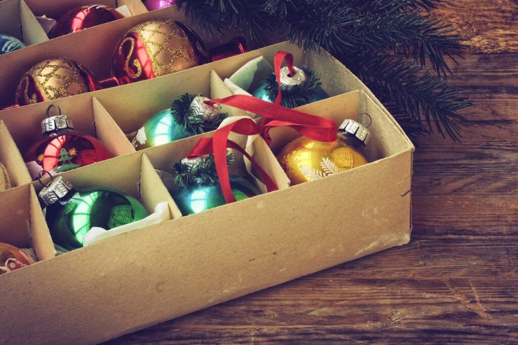 A collection of colorful, vintage ornaments arranged in a carton beneath a Christmas tree.