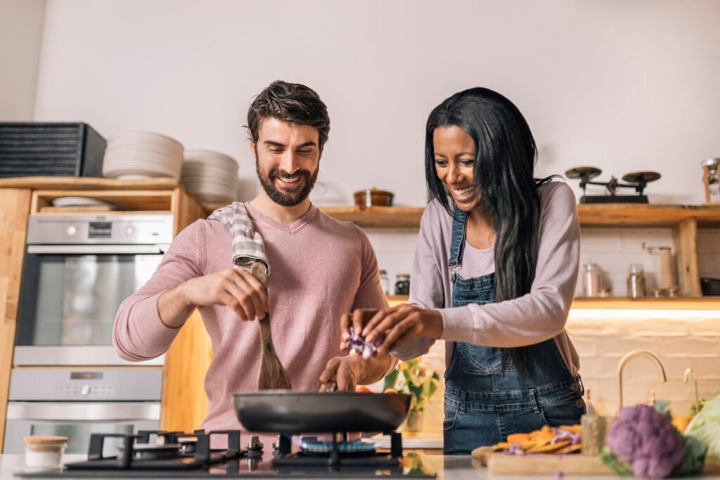 A couple gleefully cooks a meal together in a modern kitchen.