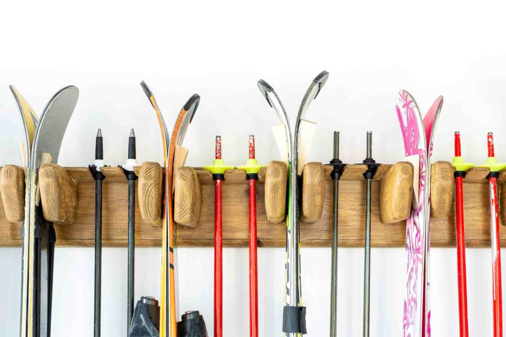 Skis and ski poles hanging on a wall-mounted wooden rack.