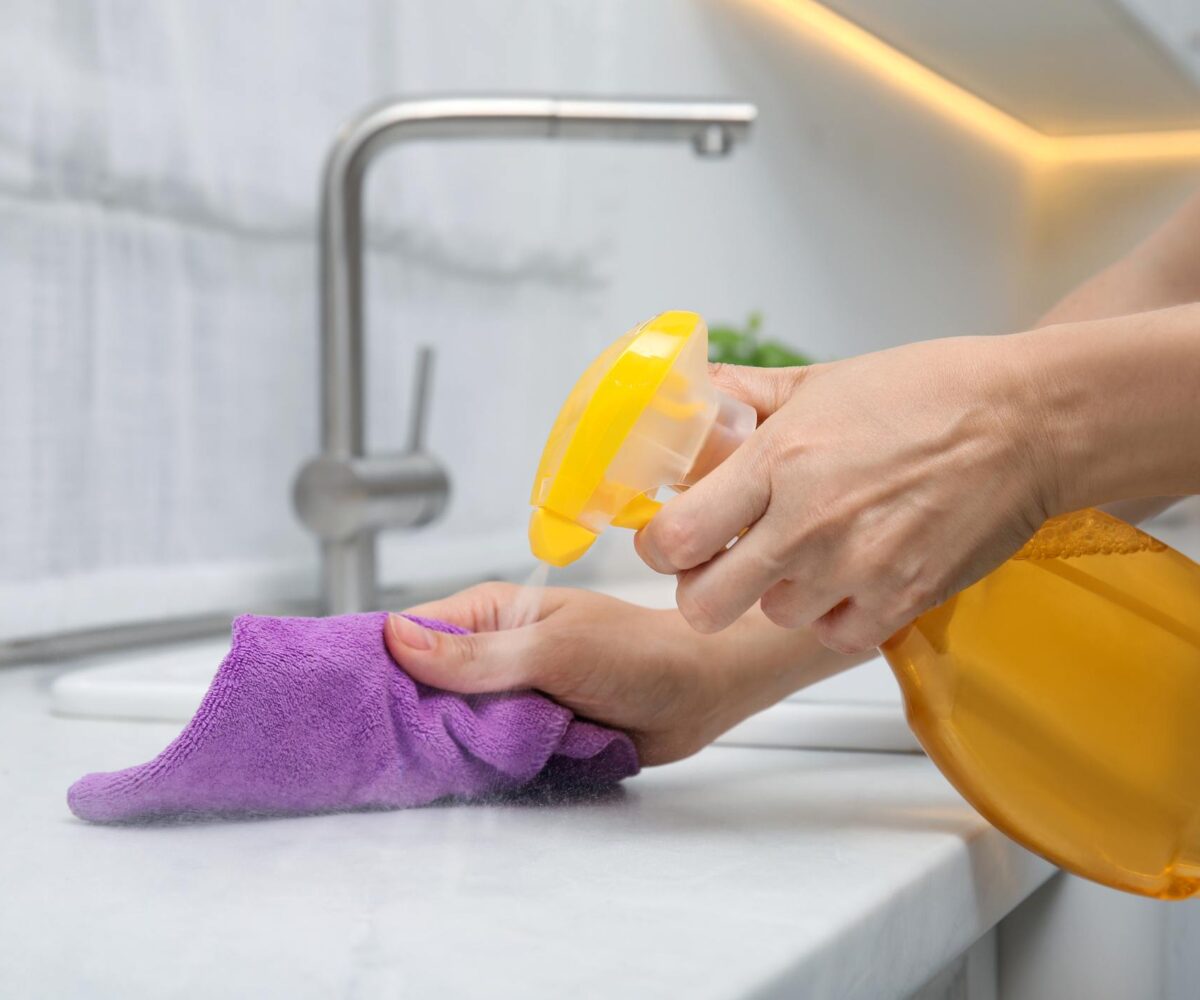 A woman cleans her white marble countertop with a rag and detergent.